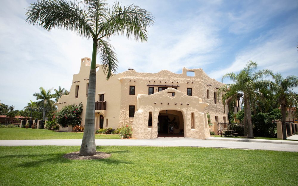 Exterior view of the Curtiss Mansion, showcasing its historic architecture with lush gardens and palm trees all around