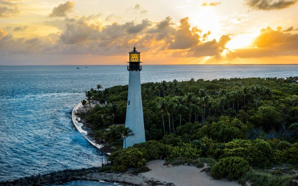 Bill Baggs Cape Florida Lighthouse against a vibrant sunset sky, with hues of orange reflecting off the calm ocean waters