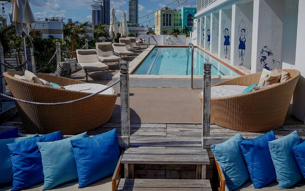 Rooftop pool area at The Local House, featuring a serene pool surrounded by lounge chairs, with panoramic views of the city skyline and partial ocean views